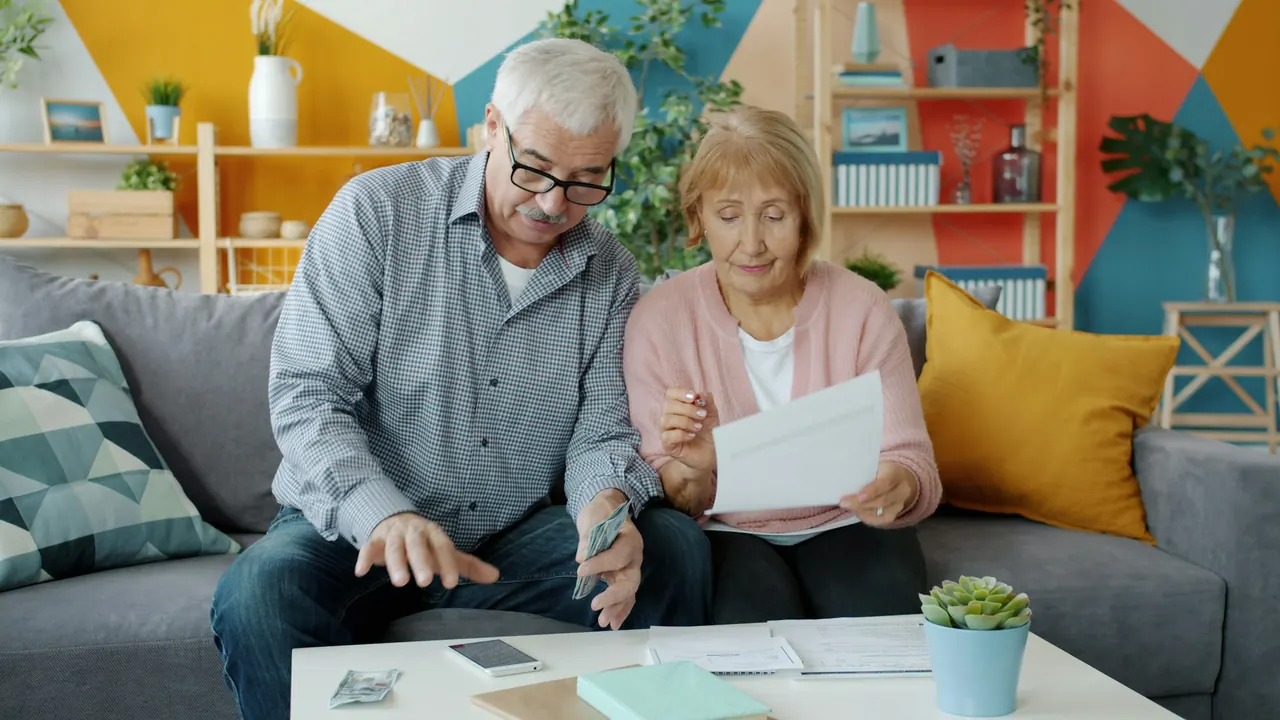An older couple sitting on a sofa reading through paperwork together