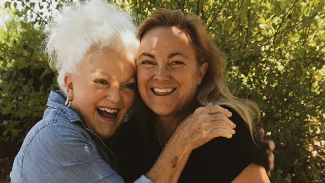 An older mother and her adult daughter hugging and laughing outdoors