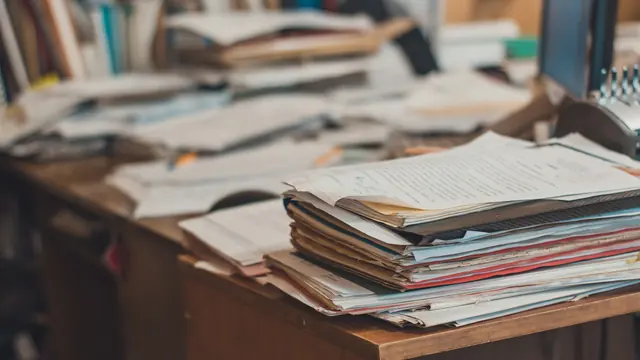 Untidy stacks of paperwork and folders piled on a desk