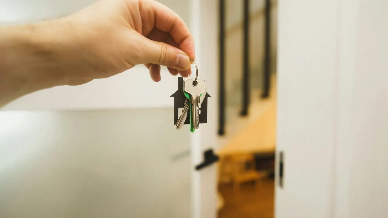 A hand holding a set of house keys on a house-shaped keyring