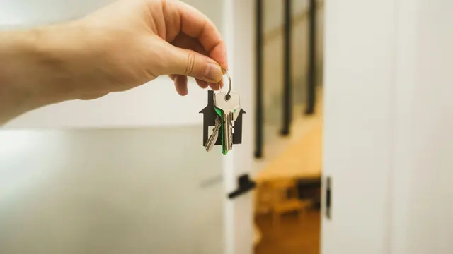 A hand holding a set of house keys on a house-shaped keyring